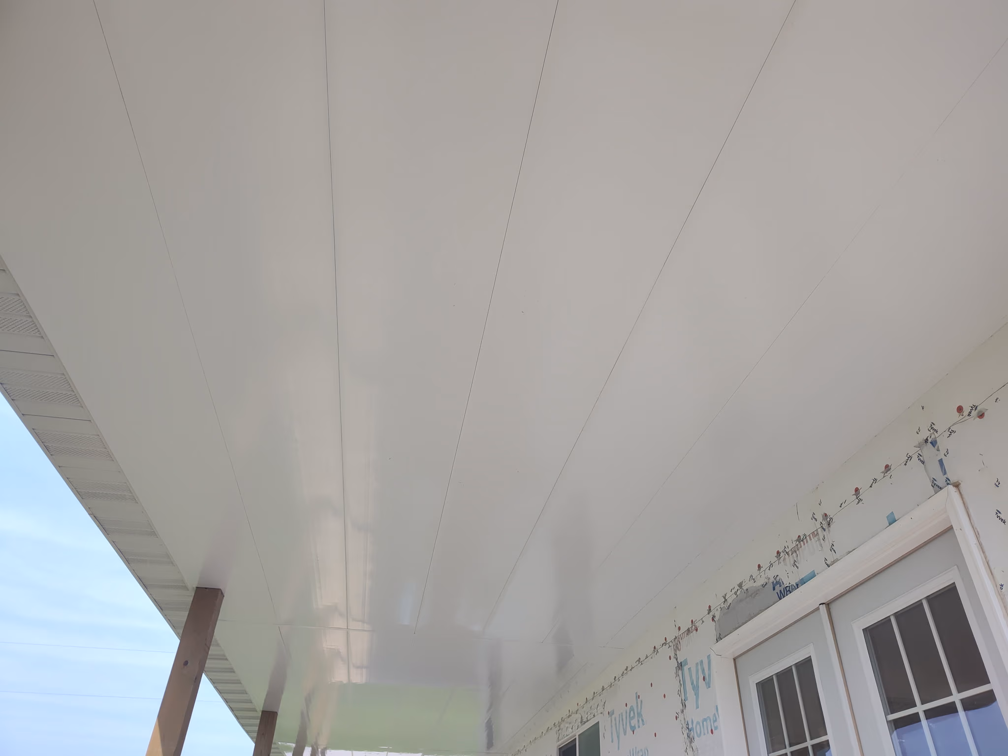 White paneled ceiling of an outdoor porch under construction with wooden support posts.