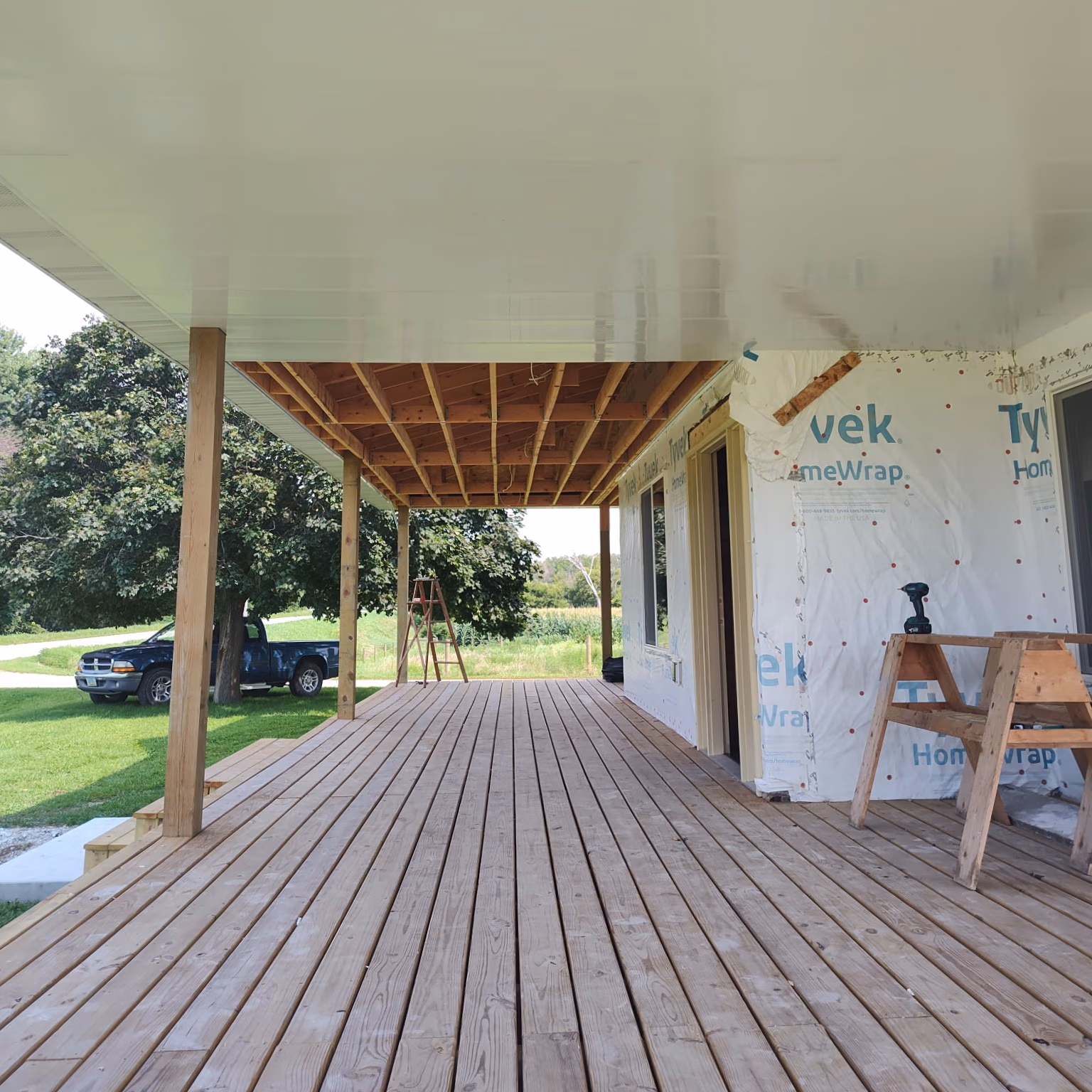New porch under construction with wooden deck, ceiling, and Tyvek home wrap on the wall.