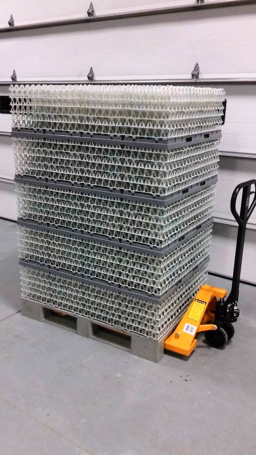 Stack of multiple plastic trays on a pallet jack in a warehouse setting.