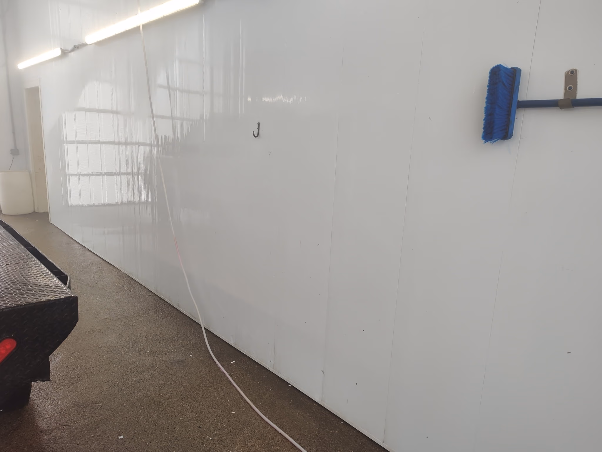 White wall with blue broom hanging and a black metal platform on the left side.