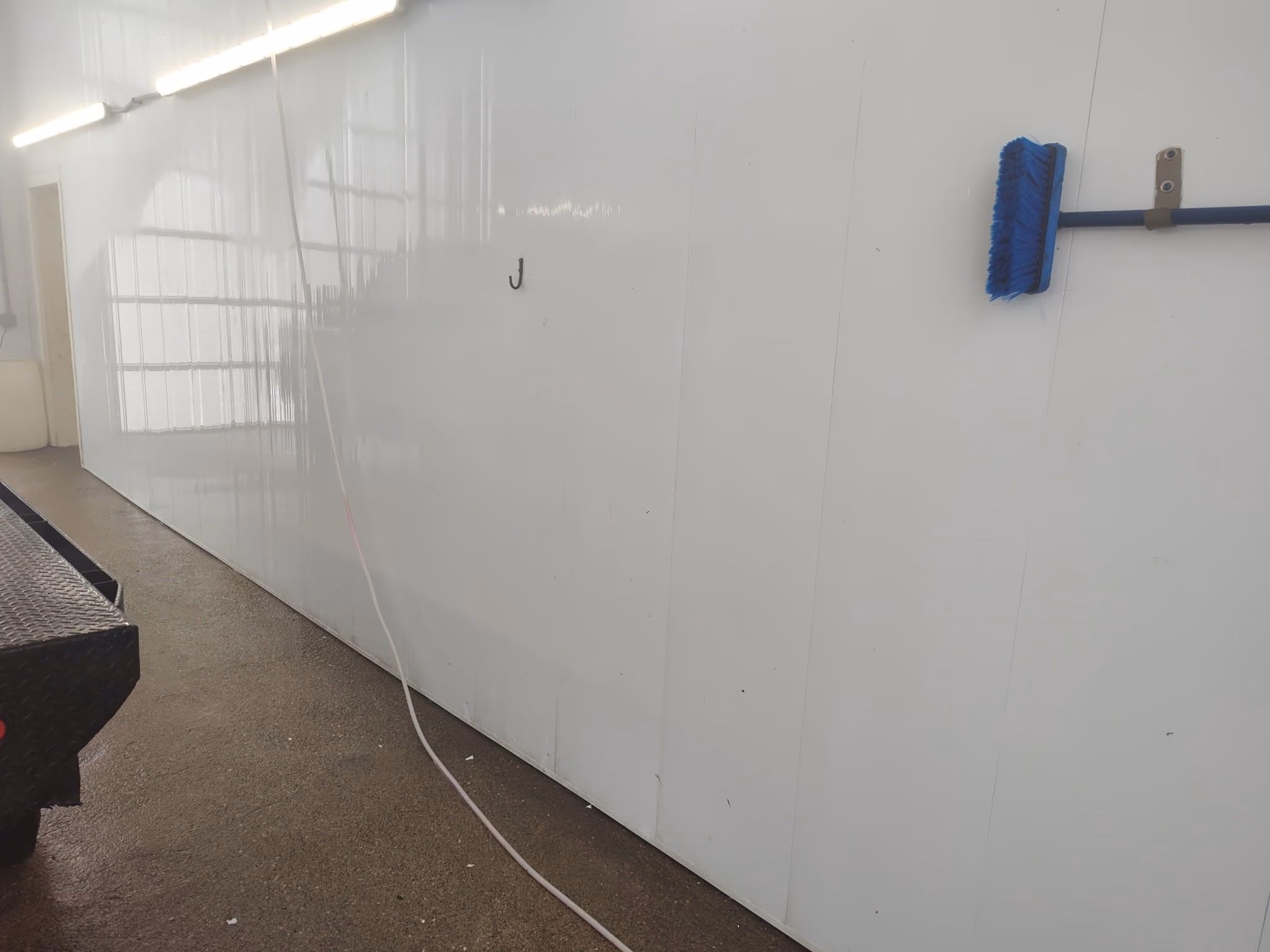 White wall with a blue broom hanging and a loose cable on the ground in an indoor space.