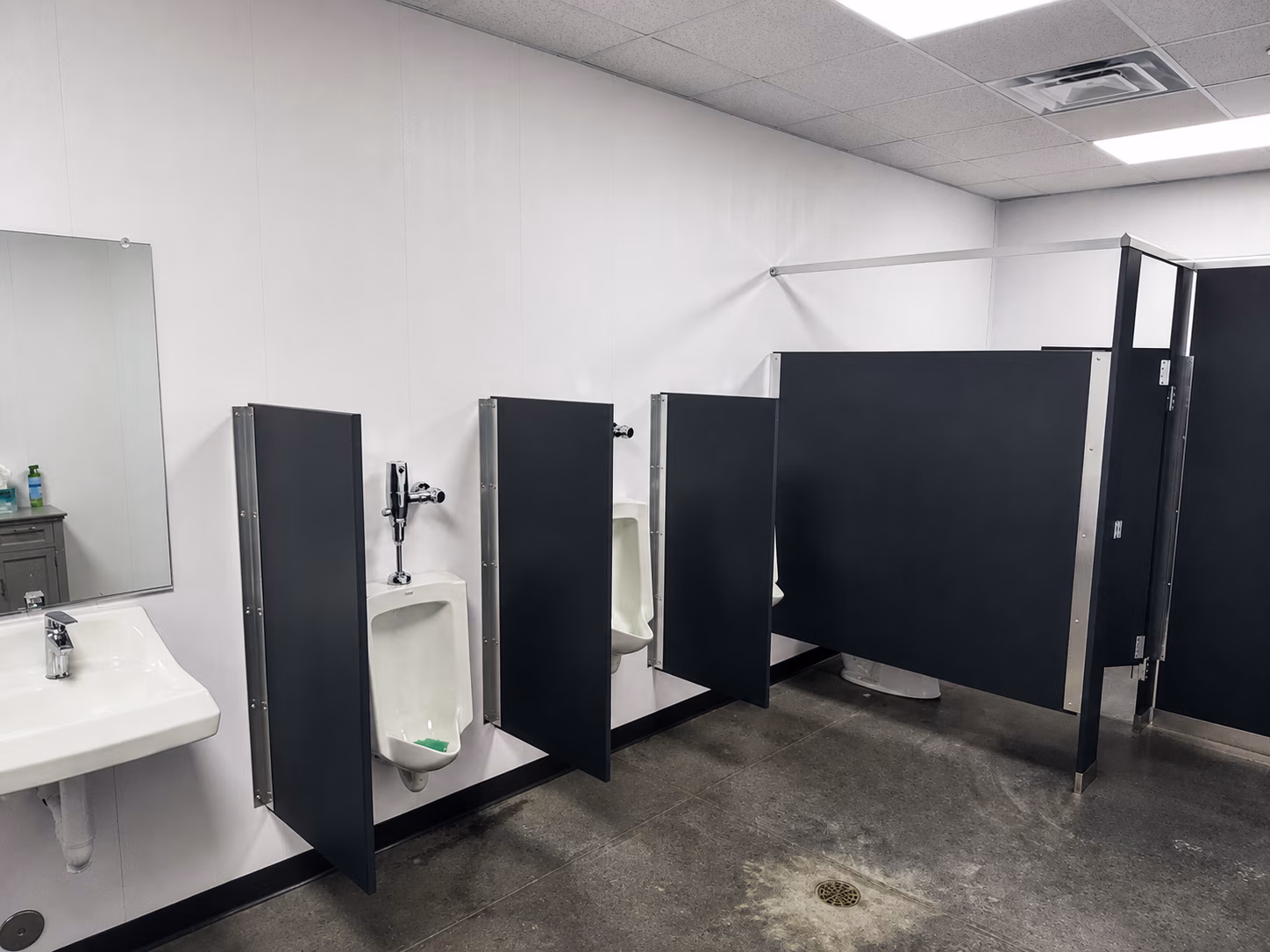 Public restroom with two urinals each with privacy panels and a stall with a closed door next to a sink.